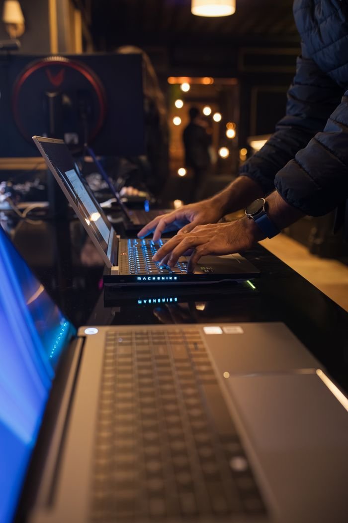 service-02 An individual typing on a laptop in a dimly lit modern workspace, emphasizing technology and focus.